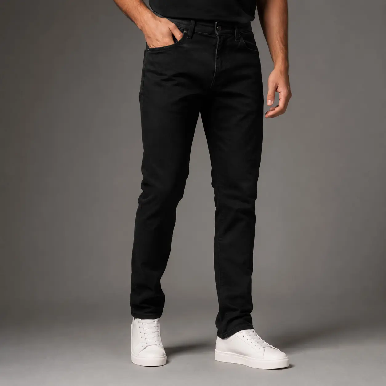 Man wearing jet black slim-fit denim jeans in a professional studio setting, front view with focus on the jeans and upper body cropped out.